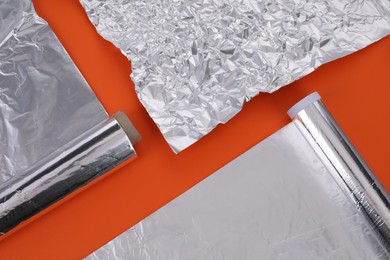 Photo of Different rolls of aluminum foil on orange background, flat lay