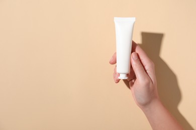 Photo of Woman with tube of hand cream on beige background, top view. Space for text