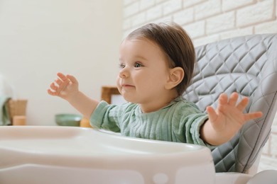 Photo of Cute little baby sitting in high chair indoors