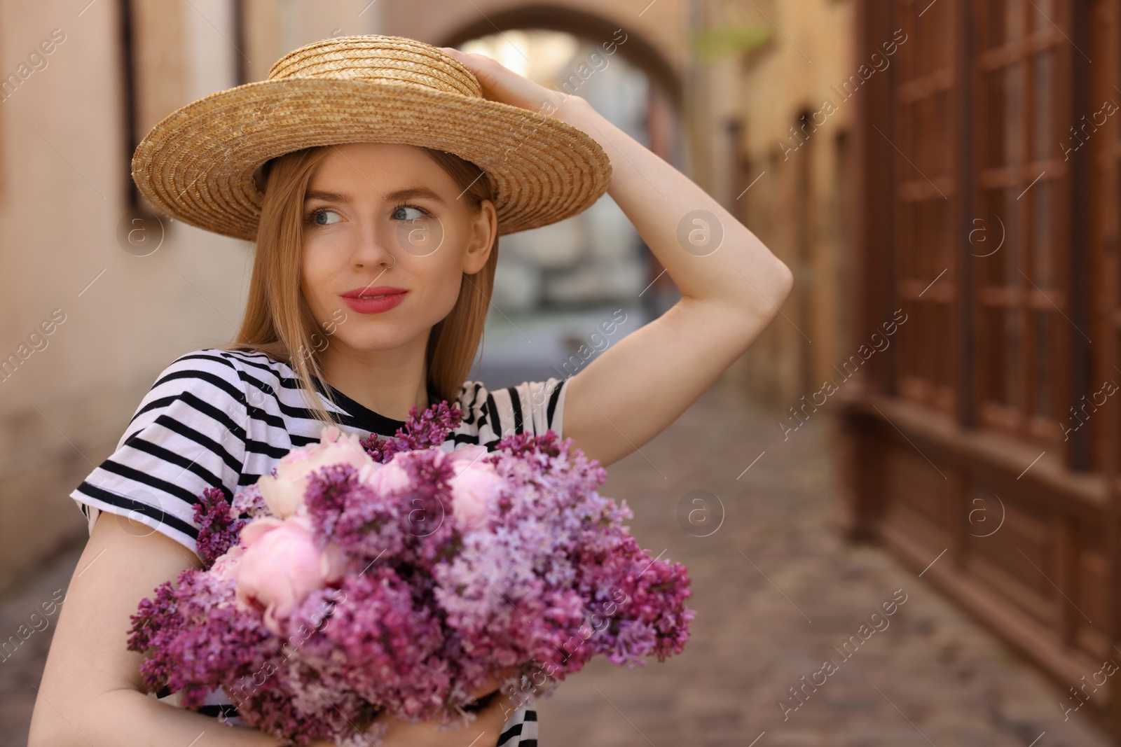 Photo of Beautiful woman with bouquet of spring flowers on city street, space for text