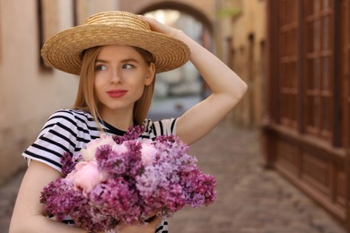 Beautiful woman with bouquet of spring flowers on city street, space for text