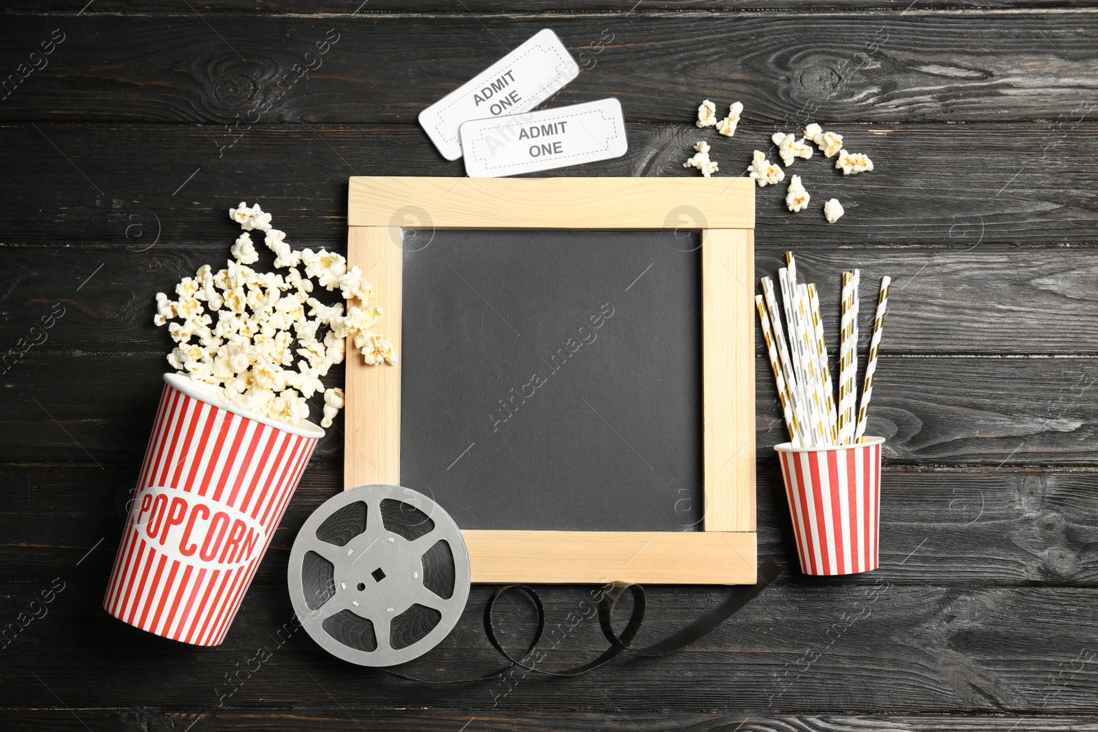 Photo of Flat lay composition with blackboard, popcorn and reel on wooden background, mockup for design. Watching cinema