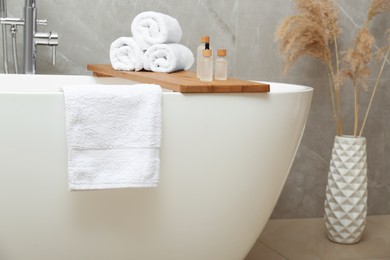 Photo of Rolled bath towels and personal care products on tub tray in bathroom