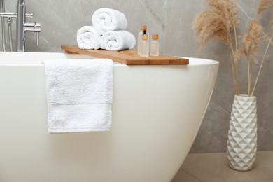 Rolled bath towels and personal care products on tub tray in bathroom