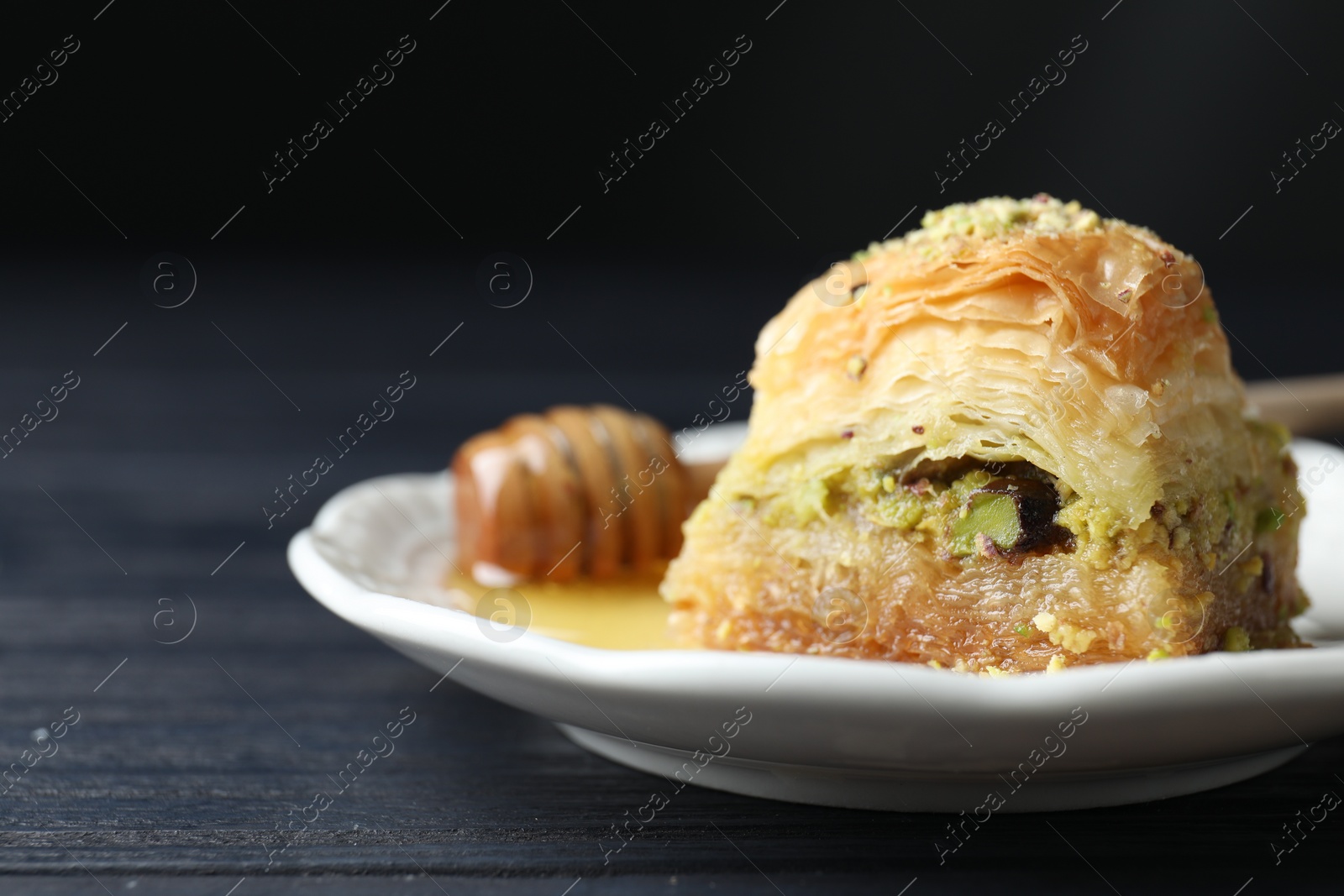 Photo of Delicious fresh baklava with chopped nuts and honey on black wooden table, closeup with space for text. Eastern sweets