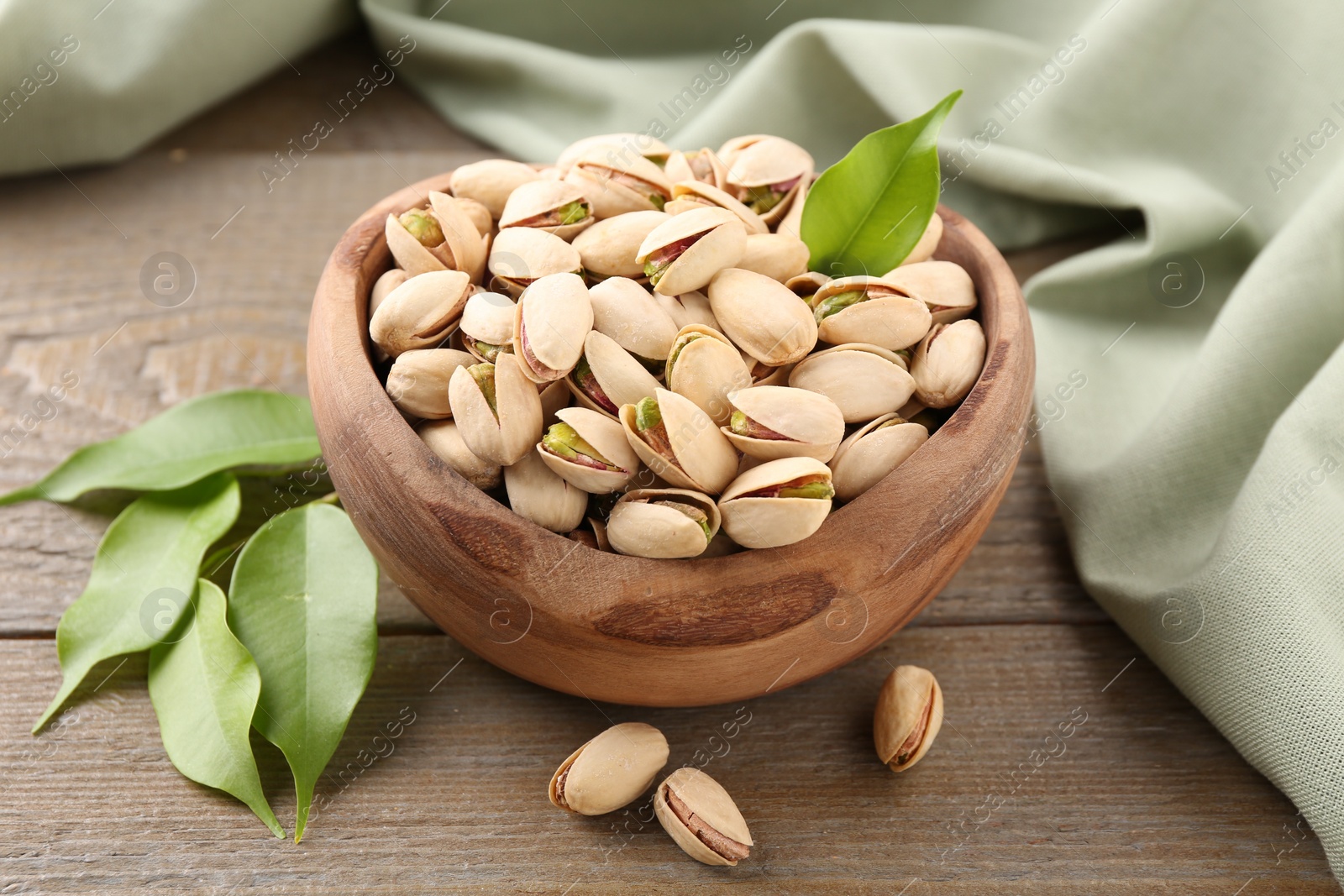 Photo of Delicious pistachios in bowl on wooden table, closeup