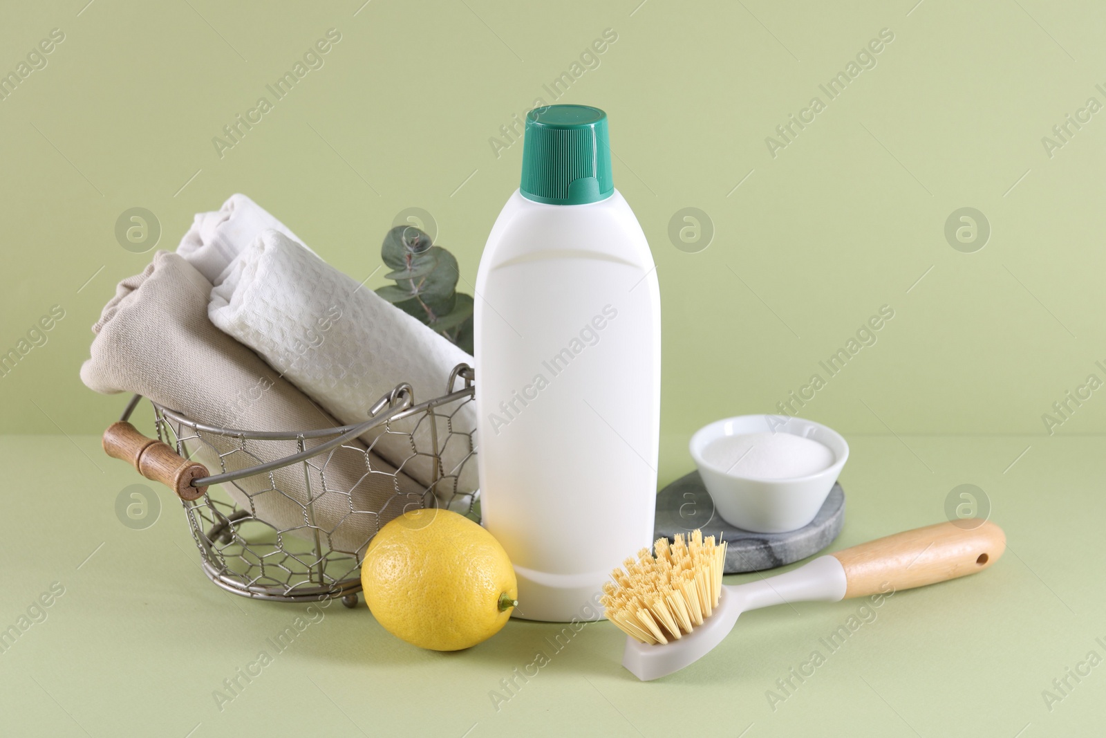 Photo of Bottle of cleaning product, baking soda, lemon and brush on light green background