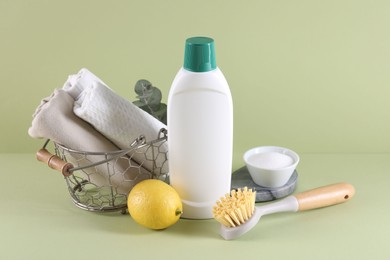 Bottle of cleaning product, baking soda, lemon and brush on light green background