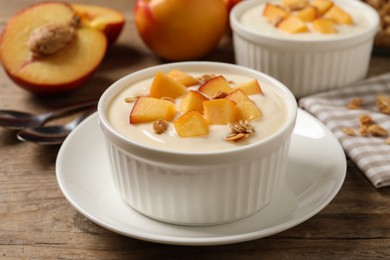 Photo of Tasty peach yogurt with granola and pieces of fruit in bowl on wooden table