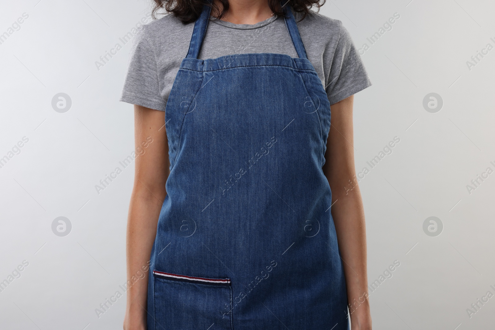 Photo of Woman wearing kitchen apron on light grey background, closeup. Mockup for design