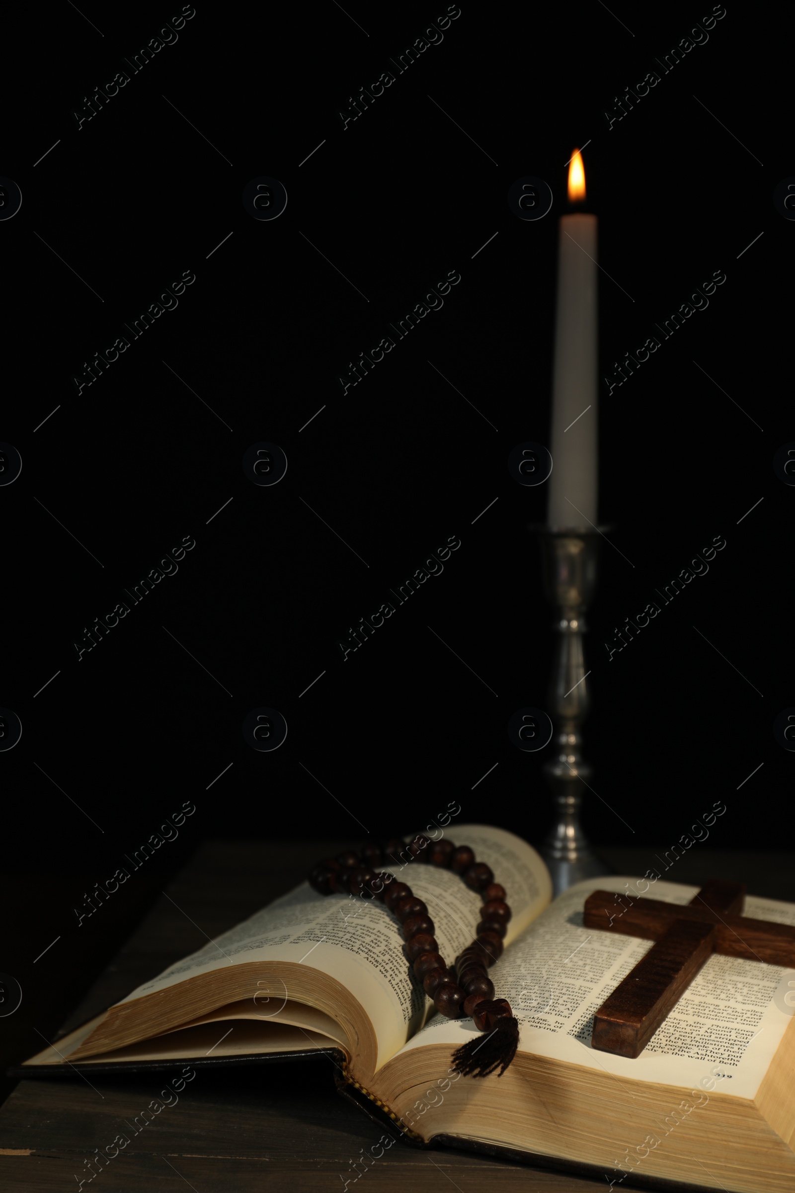 Photo of Church candle, Bible, rosary beads and cross on wooden table against black background, space for text