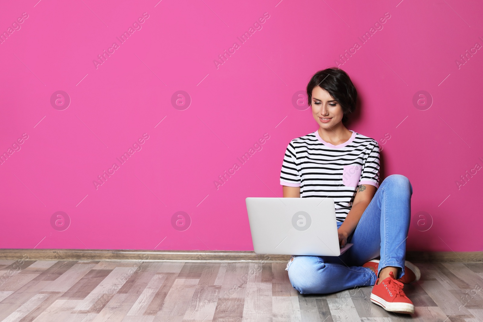 Photo of Young woman with modern laptop sitting on floor near color wall