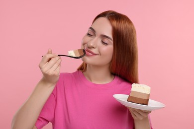 Young woman eating piece of tasty cake on pink background