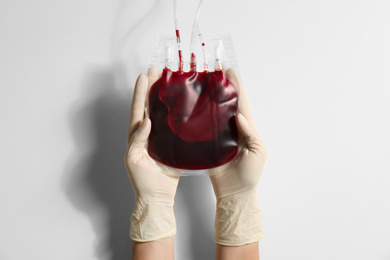 Woman holding blood for transfusion on light background, closeup. Donation concept