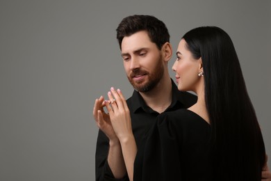 Photo of Man putting elegant ring on woman's finger against dark grey background