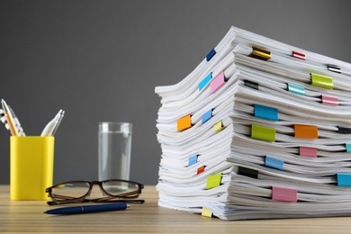 Photo of Stack of documents with binder clips and glasses on wooden table against grey background