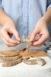 Photo of Woman peeling fresh shrimp at table, closeup