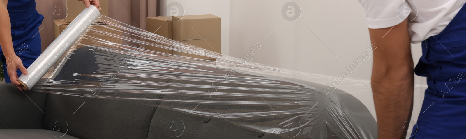 Image of Workers wrapping sofa in stretch film indoors, closeup. Banner design