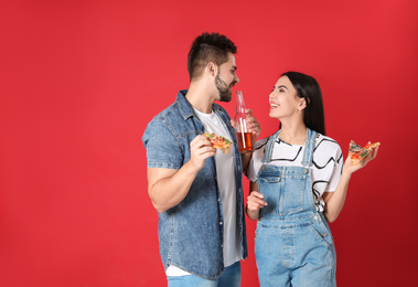 Happy young couple with pizza and beer on red background, space for text