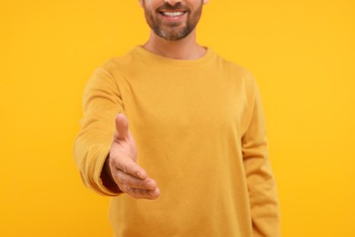 Man welcoming and offering handshake on orange background, closeup