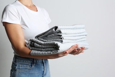 Photo of Woman holding stack of clean bed linens on light grey background