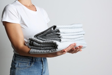 Woman holding stack of clean bed linens on light grey background