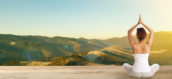 Young African American woman practicing yoga on wooden surface against beautiful mountain landscape, space for text. Banner design