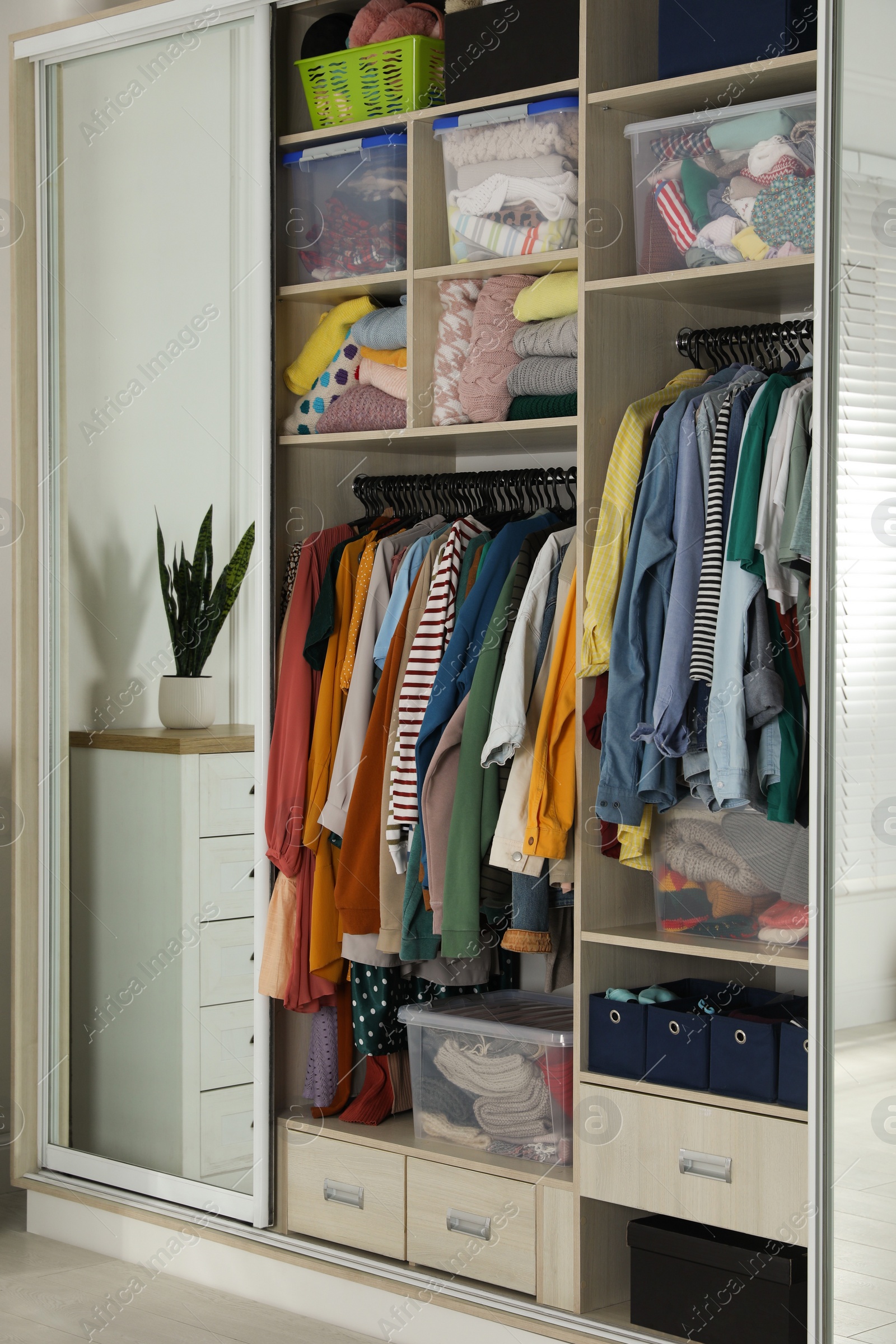 Photo of Wardrobe closet with different stylish clothes and home stuff in room. Fast fashion