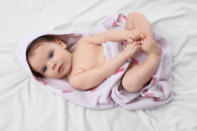 Cute little baby wrapped with hooded towel after bathing on bed, top view