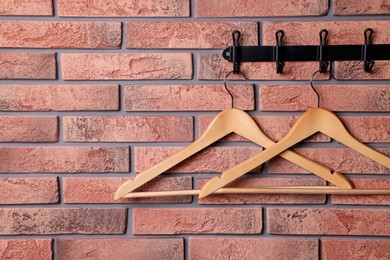 Photo of Hook rack with wooden clothes hangers on red brick wall. Space for text