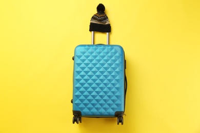 Photo of Stylish suitcase with warm hat on color background, top view