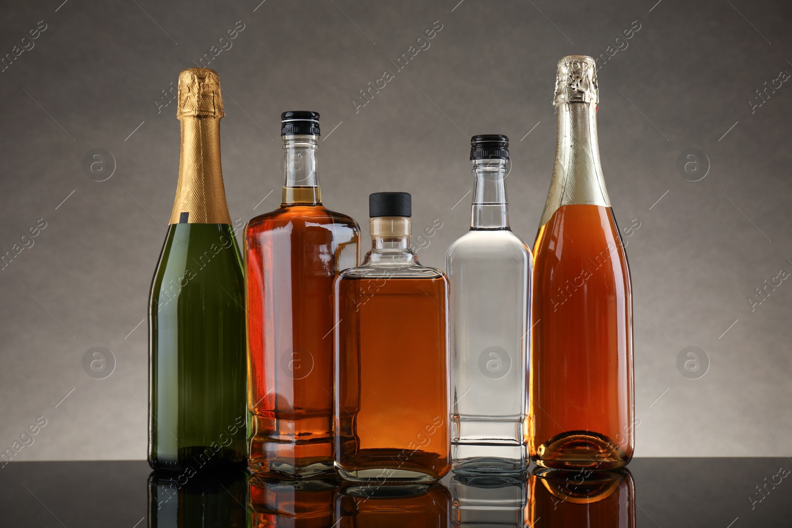 Photo of Bottles of different alcoholic drinks on table against gray background