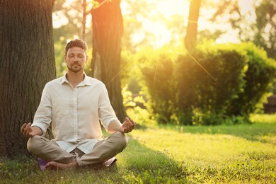 Image of Man meditating in park on sunny morning. Practicing yoga