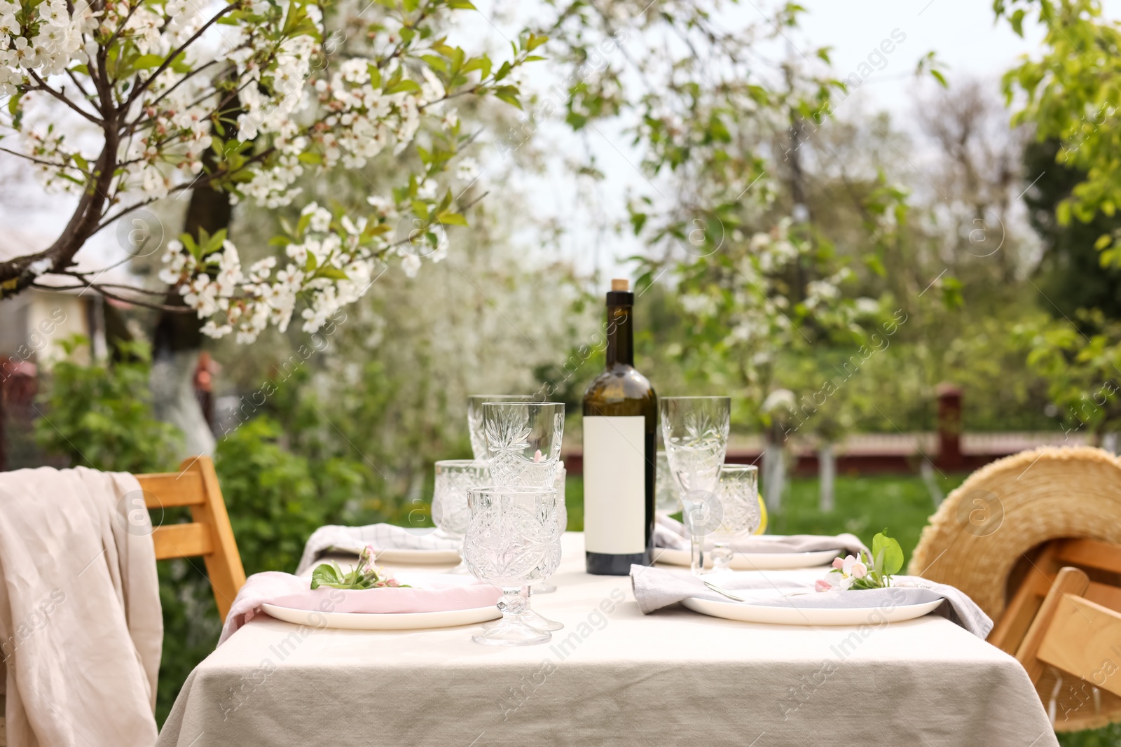 Photo of Stylish table setting with beautiful spring flowers, wine, plates and glasses in garden