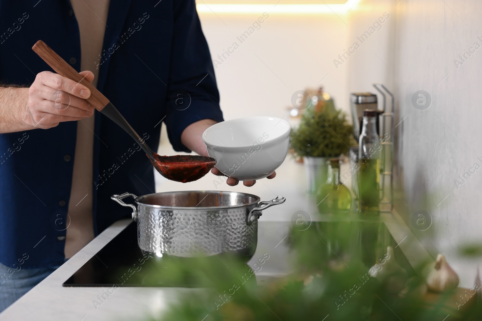 Photo of Man pouring delicious tomato soup into bowl in kitchen, closeup