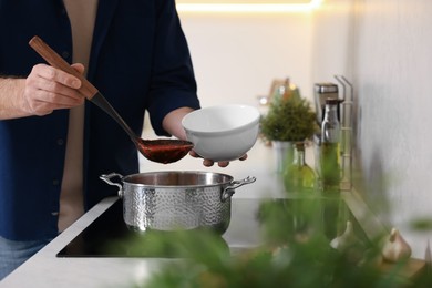 Man pouring delicious tomato soup into bowl in kitchen, closeup