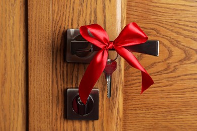 Photo of Key with red bow on door handle, closeup view. Housewarming party