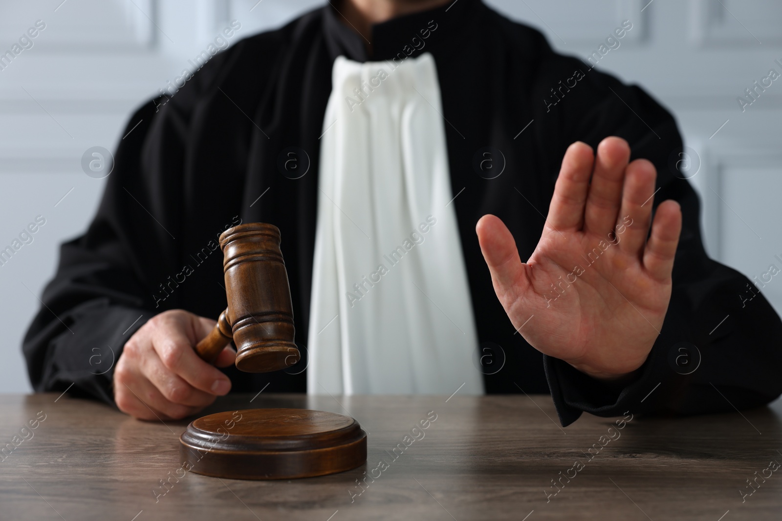 Photo of Judge with gavel showing stop gesture and sitting at wooden table indoors, closeup