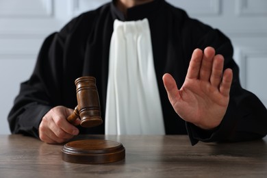 Judge with gavel showing stop gesture and sitting at wooden table indoors, closeup