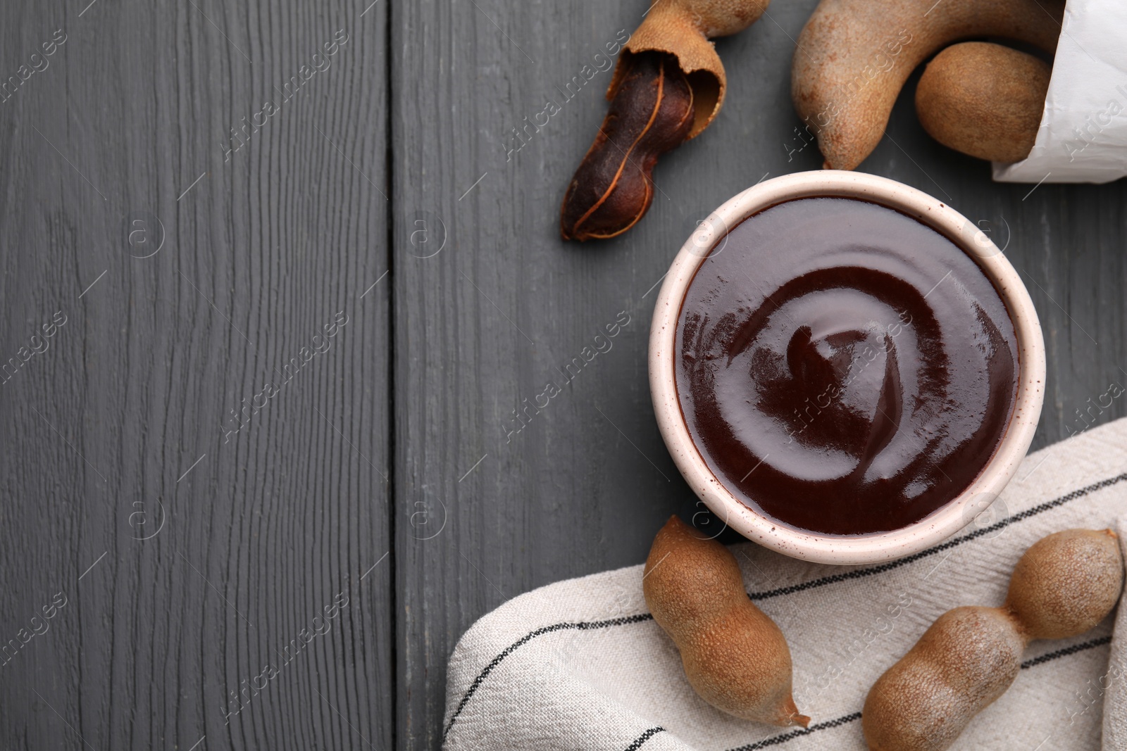 Bowl of tamarind sauce and fresh pods on grey wooden table, flat lay. Space for text Photo of Bowl of tamarind sauce and fresh pods on grey wooden table, flat lay. Space for text