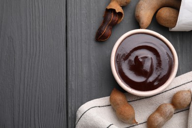 Photo of Bowl of tamarind sauce and fresh pods on grey wooden table, flat lay. Space for text
