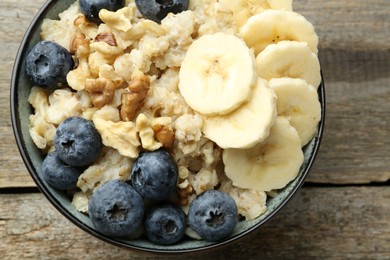 Photo of Tasty oatmeal with banana, blueberries and walnuts served in bowl on wooden table, top view