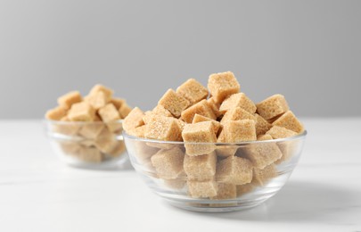 Photo of Brown sugar cubes in glass bowl on white table, closeup