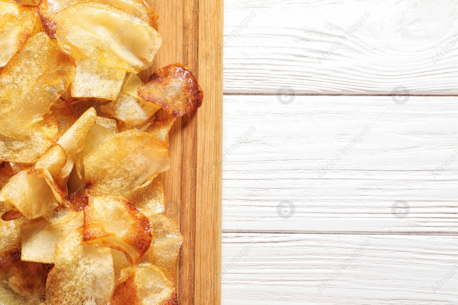 Photo of Wooden board with crispy potato chips on table, top view