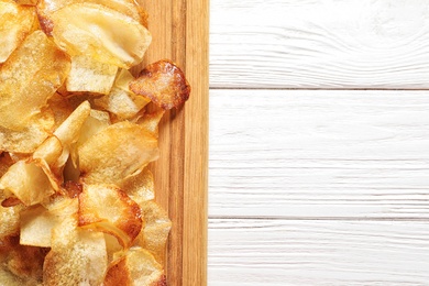 Photo of Wooden board with crispy potato chips on table, top view