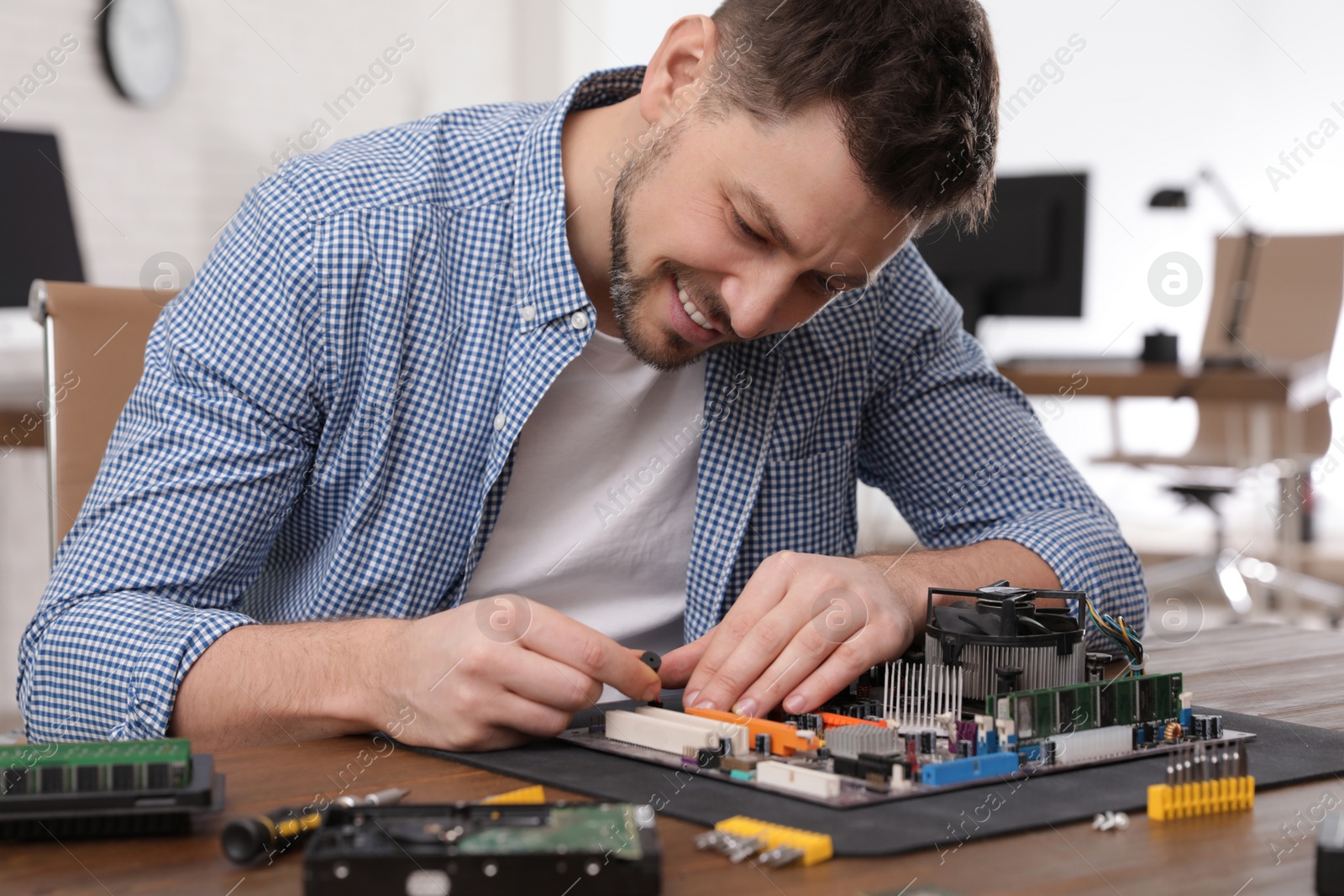 Photo of Male technician repairing motherboard at table indoors