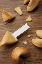 Tasty fortune cookies and paper with prediction on wooden table, flat lay. Space for text