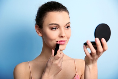 Photo of Young woman applying lipstick on color background. Professional makeup products