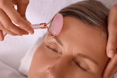 Woman receiving facial massage with rose quartz roller in beauty salon, closeup