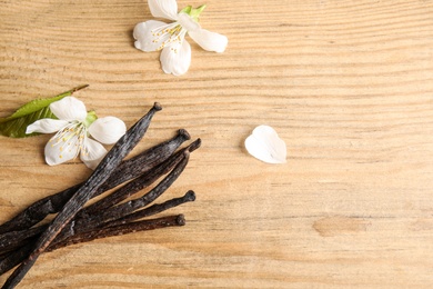 Flat lay composition with aromatic vanilla sticks and flowers on wooden background. Space for text